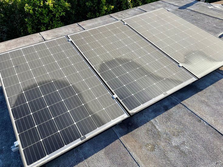 Three solar panels on a rooftop, with one panel dented, outdoors in daylight.