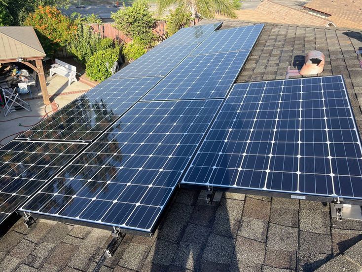 Solar panels installed on a brown shingled roof, set against a residential backyard.