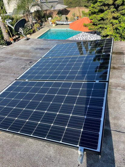 Solar panels on a concrete roof with a pool and foliage visible in the background.