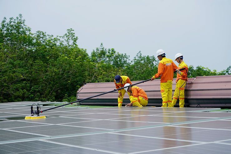Workers in orange uniforms cleaning solar panels on a roof.