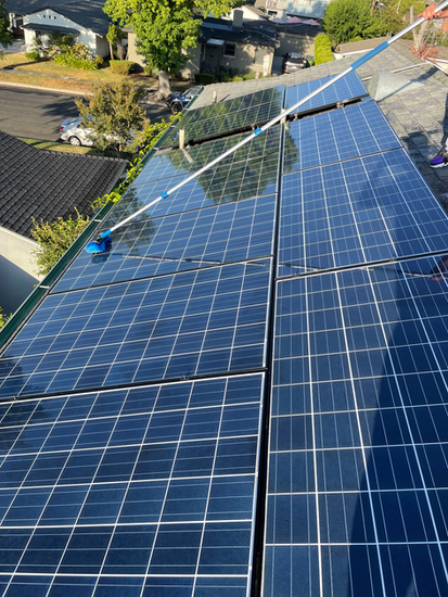 Solar panels on a rooftop, being cleaned with a long-handled brush, sunny day.