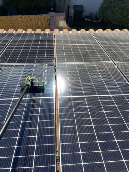 Cleaning solar panels on a rooftop with a long-handled brush; sunny day.