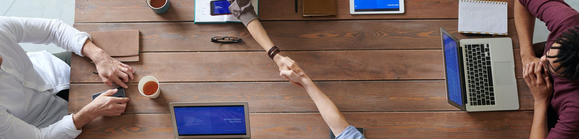 A group of people are shaking hands over a wooden table.