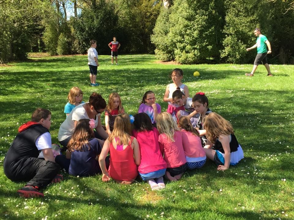 A group of children are sitting in a circle on the grass in a park.