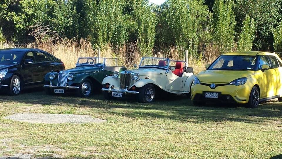 Three old cars are parked next to each other in a grassy field.