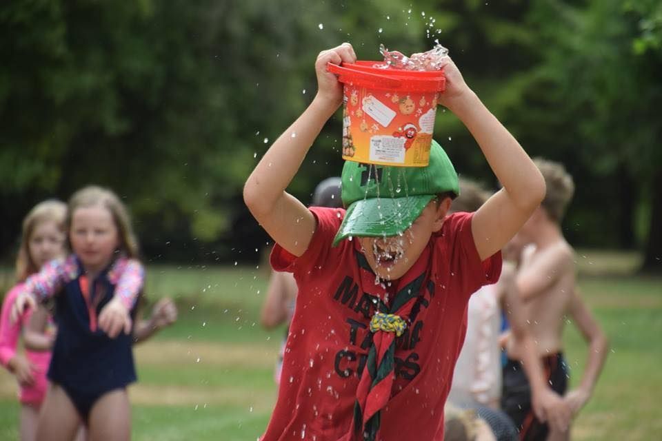 A boy in a red shirt is holding a bucket of water over his head.