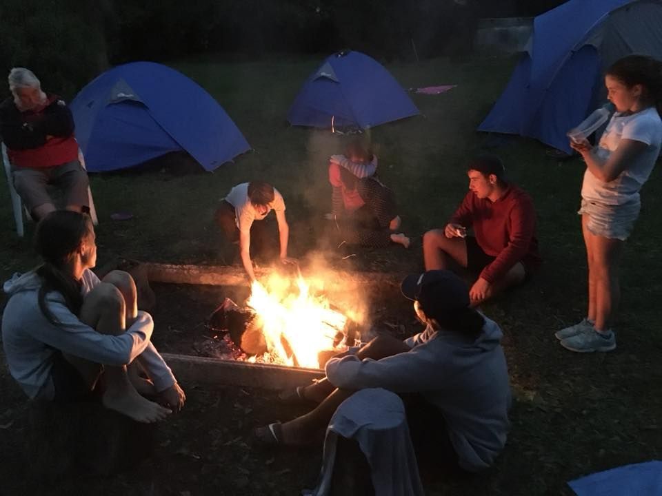 A group of people sit around a campfire with tents in the background