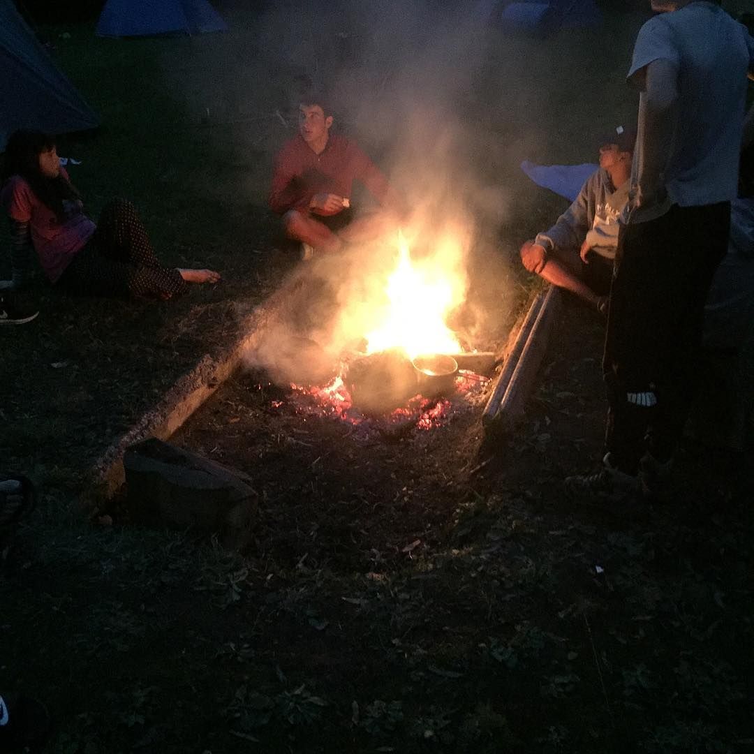 A group of people are sitting around a campfire at night.