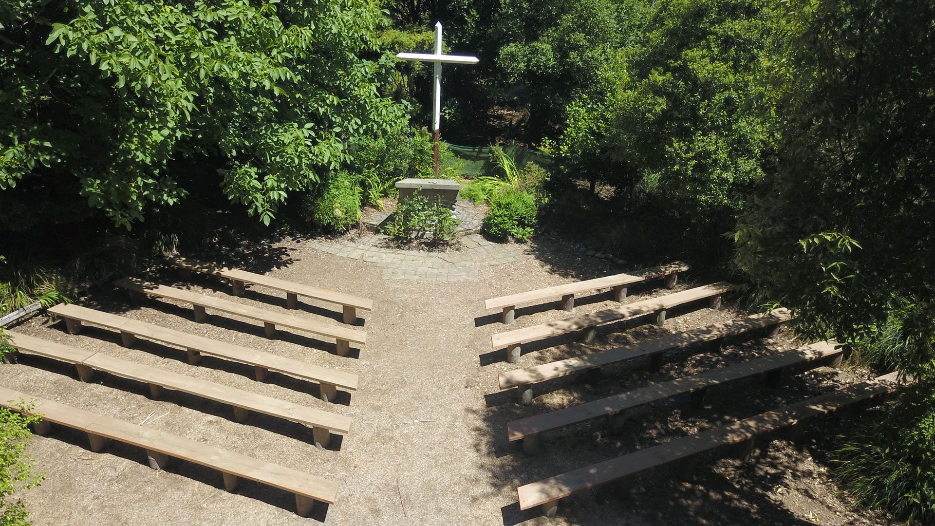 An aerial view of a small church with a cross in the middle surrounded by trees.