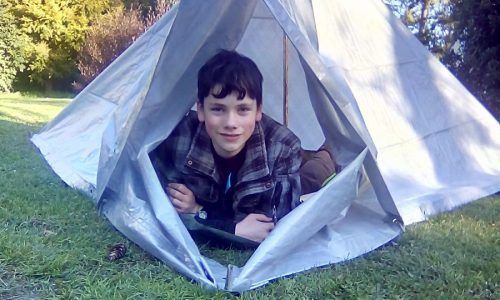 A young boy is laying in a tent on the grass.