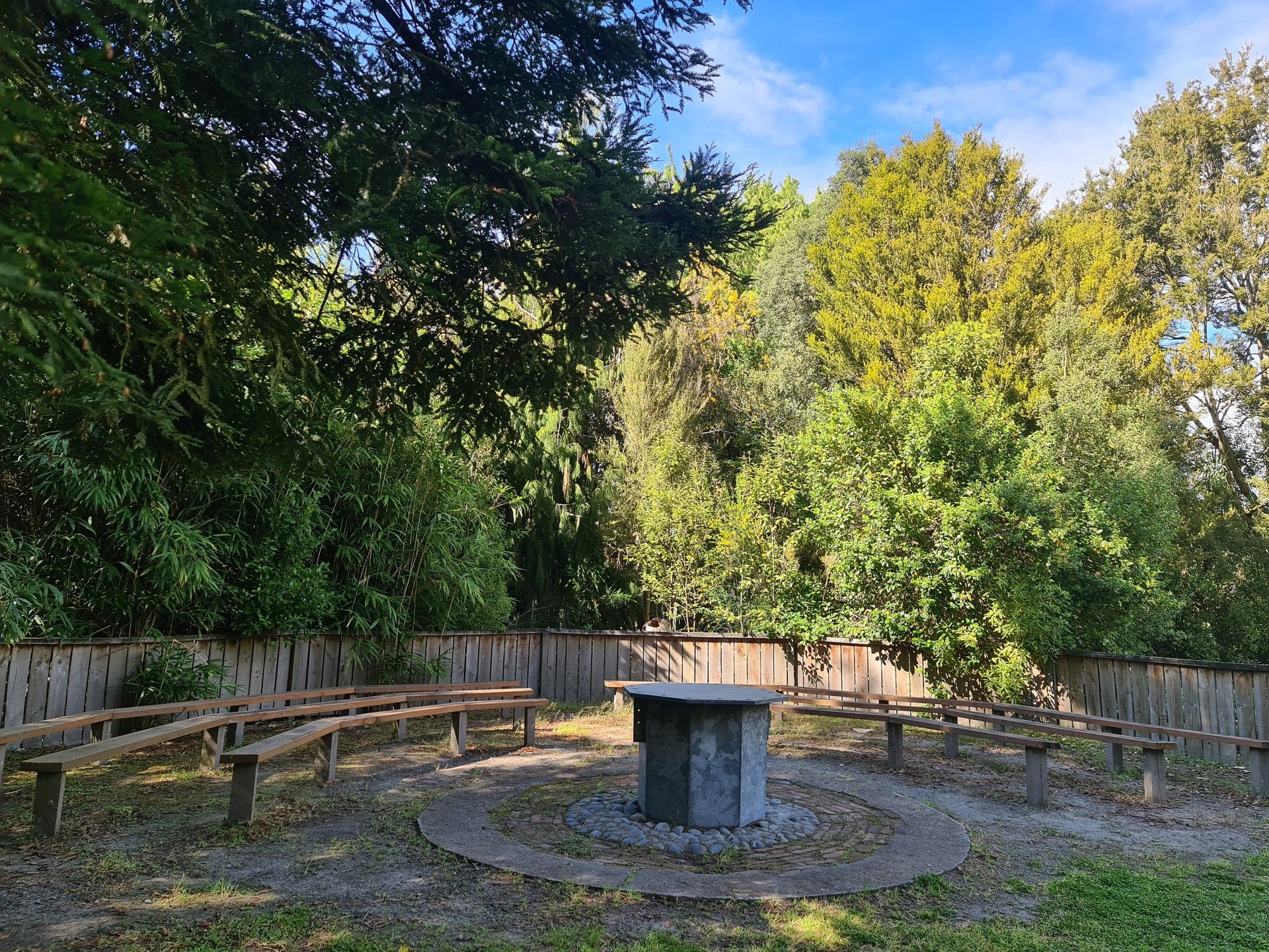 A circle of benches around a table in the middle of a forest.