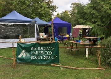 A group of tents and tables in a field with a sign that says bishopsall harewood scout group.