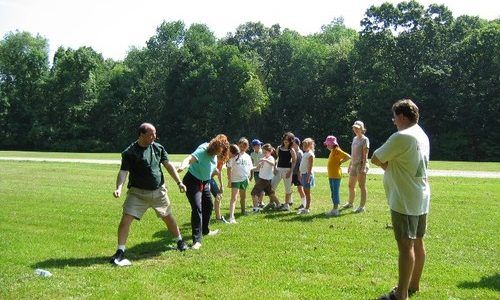 A group of people are standing in a grassy field while a man stands in the foreground