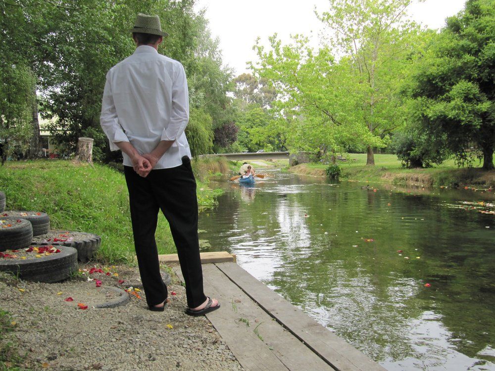 A man in a hat stands on a dock looking at a river