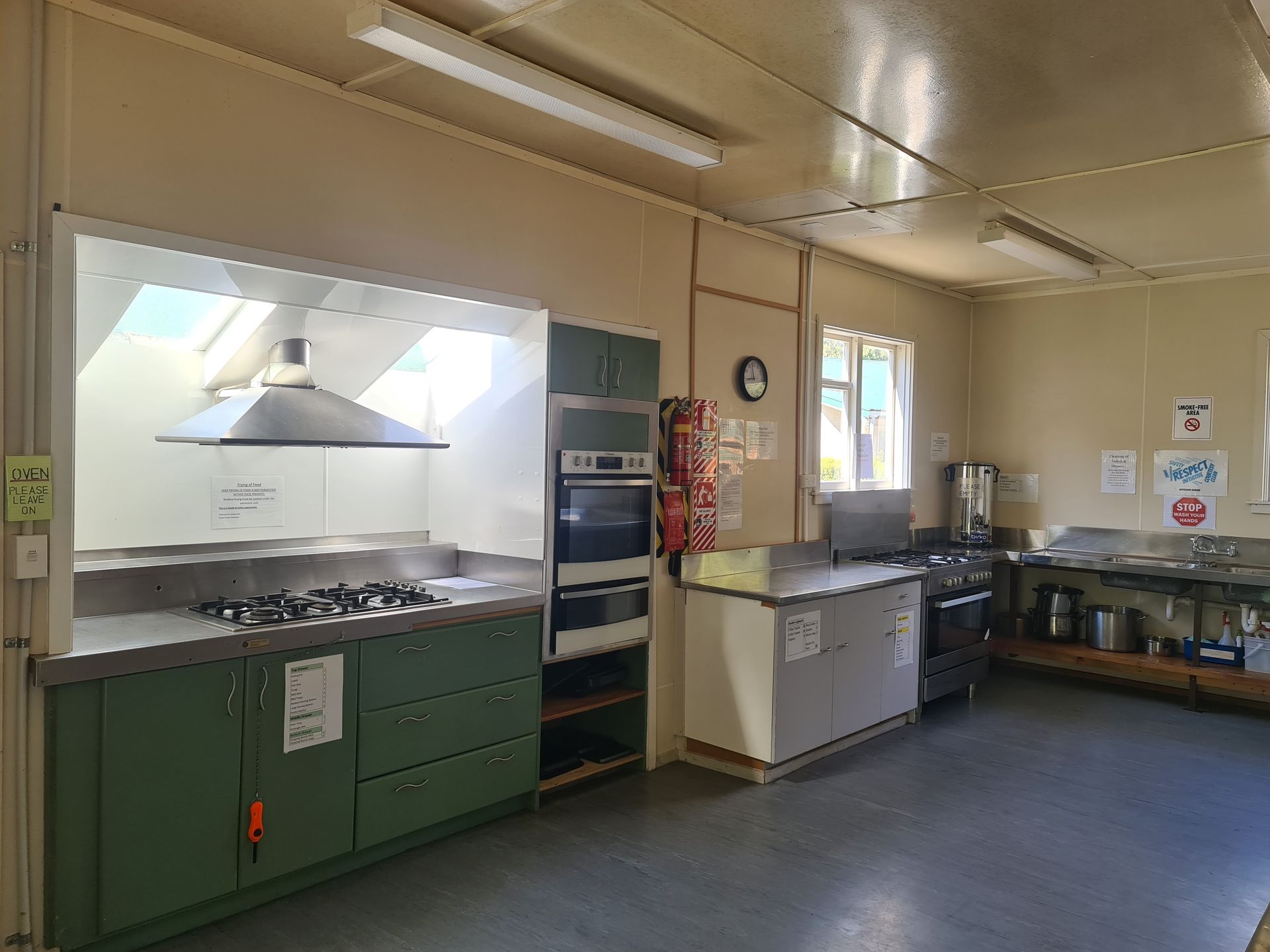 A kitchen with green cabinets , a stove , an oven , and a window.