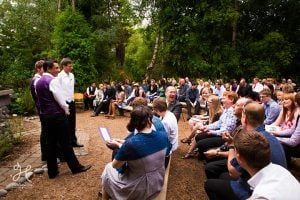 A group of people are sitting in chairs at a wedding ceremony in the woods.