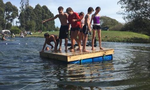 A group of children are standing on a raft in the water.