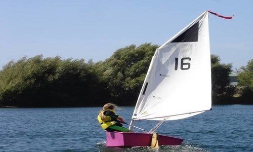 A person is sailing a small boat with the number 16 on the sail