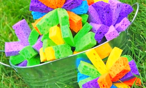 A bucket filled with colorful sponges sitting on top of a lush green field.