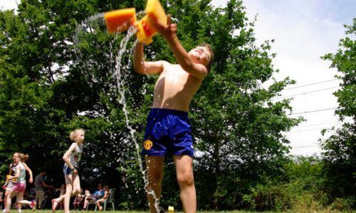 A young boy is pouring water from an orange bucket into his face.