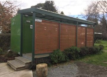 A green building with a wooden fence around it is in a park.