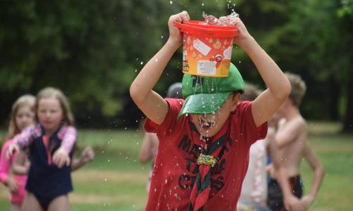 A young boy is pouring water from a bucket on his head.