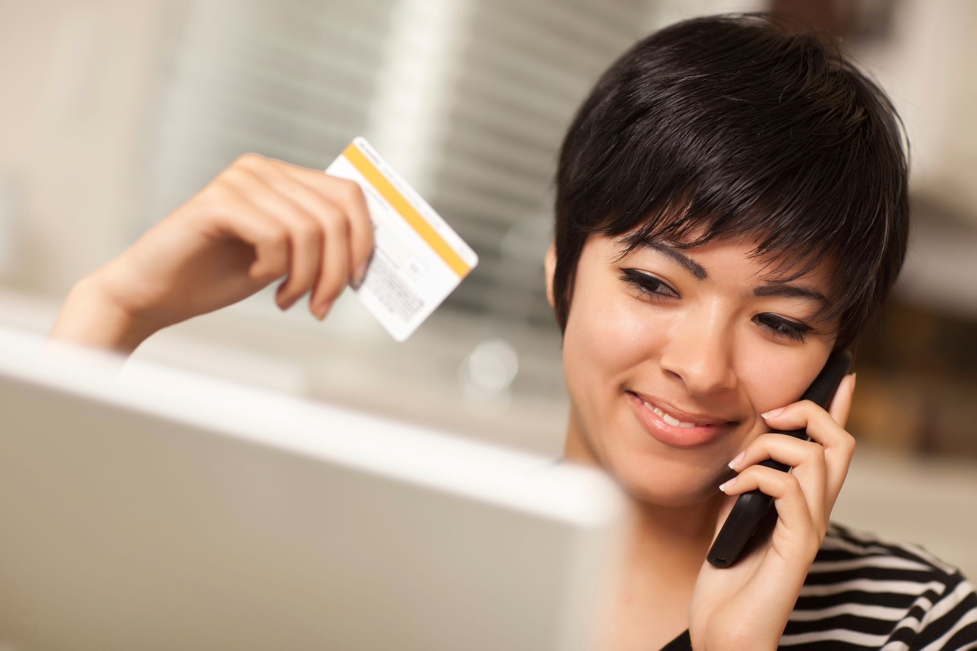 A woman is holding a credit card while talking on a cell phone.