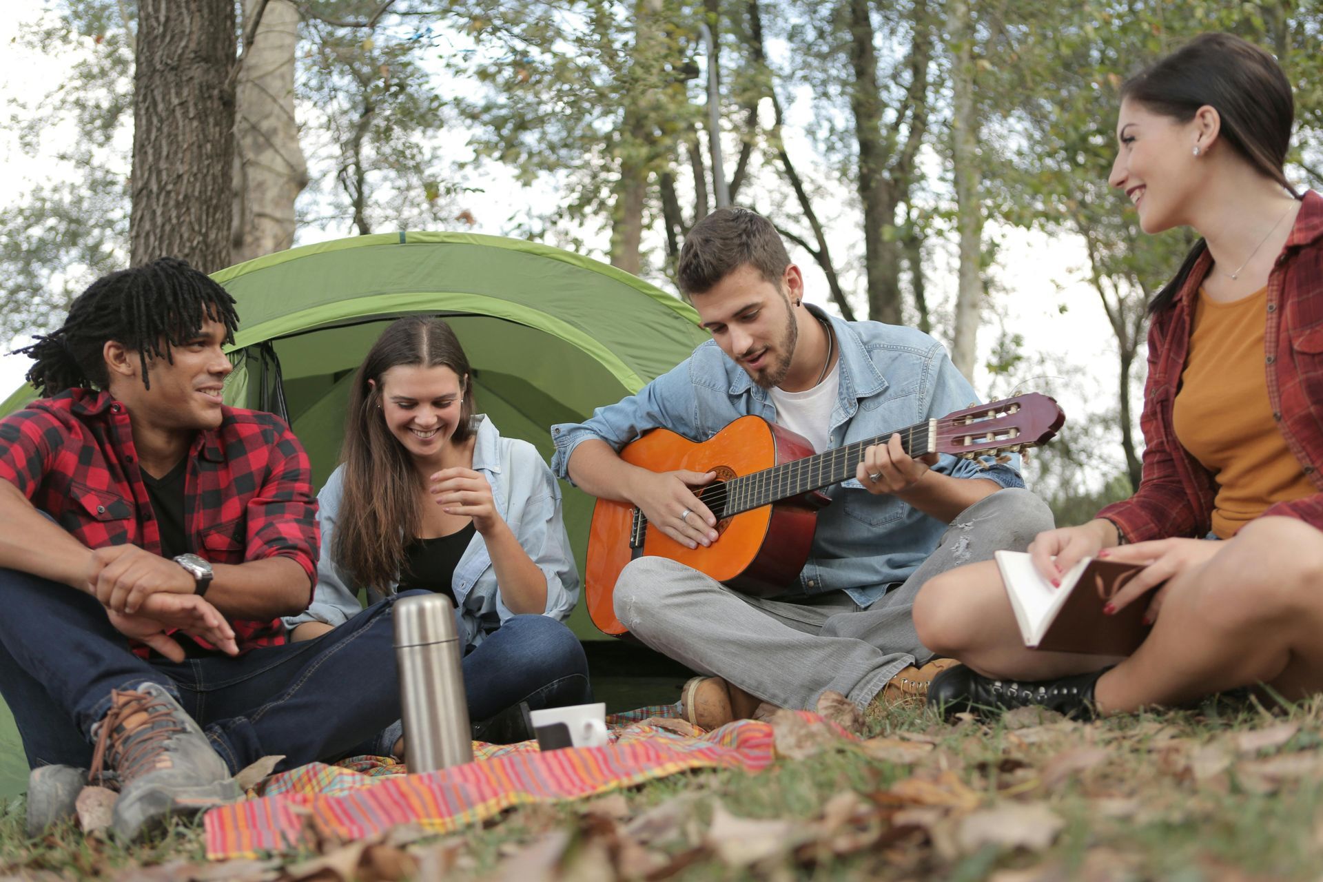 A group of people are sitting in front of a tent playing guitars.