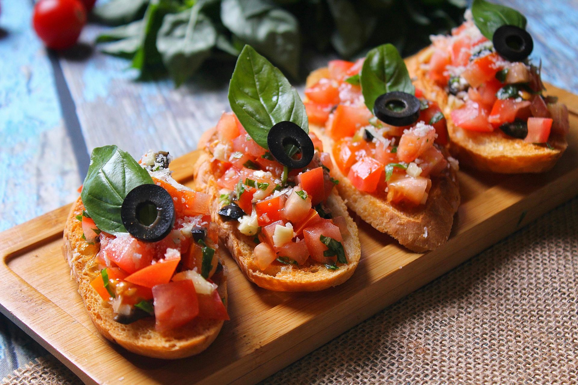 A wooden cutting board topped with slices of bread topped with tomatoes and olives.