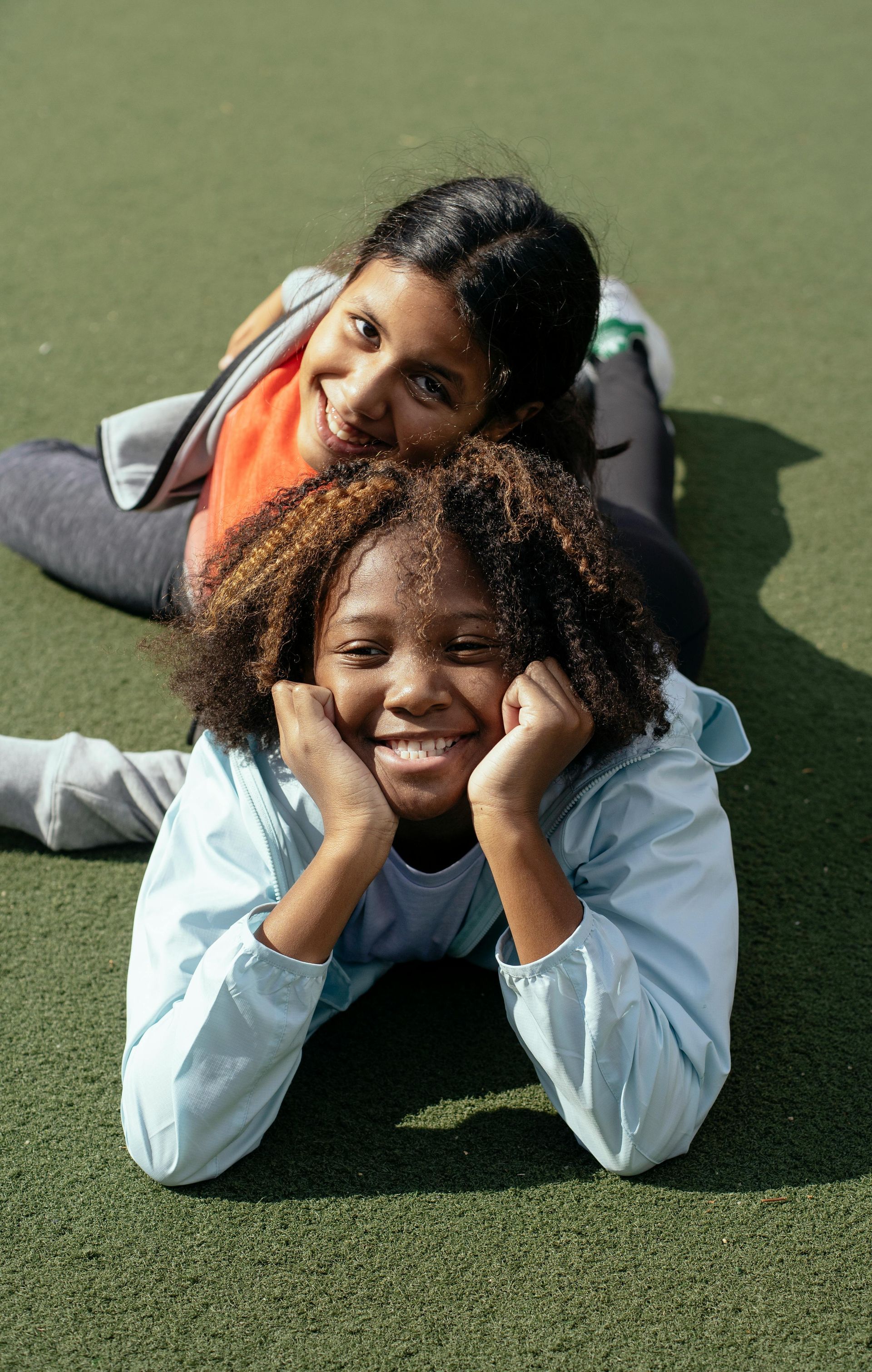 Two young girls are laying on the grass together and smiling.