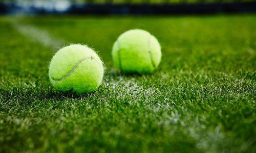 Two tennis balls are sitting on the grass on a tennis court.