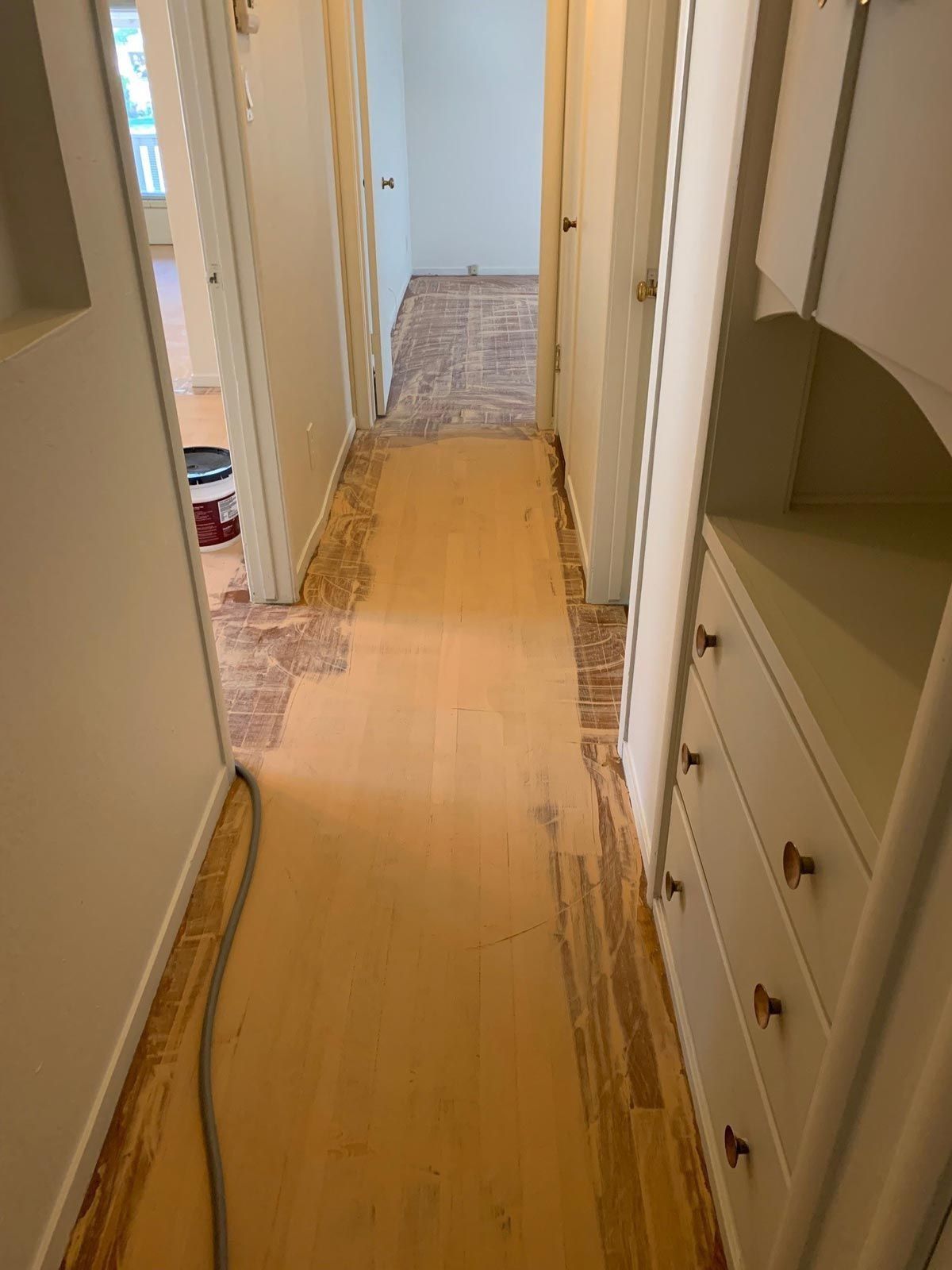 Hallway with exposed wood flooring during renovation; cream walls, built-in cabinet.