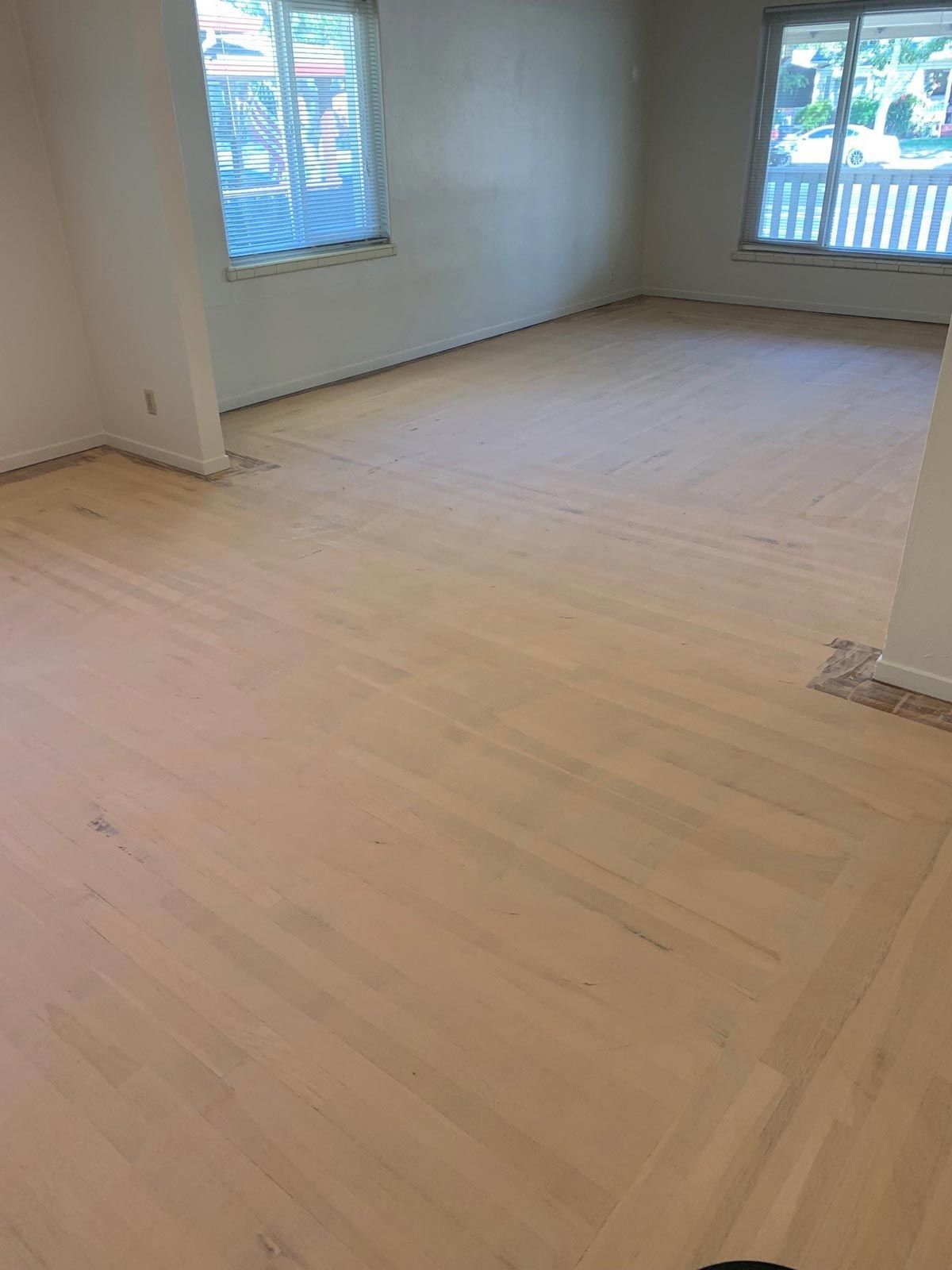 Empty room with light-colored hardwood floors and two windows. White walls and natural light.
