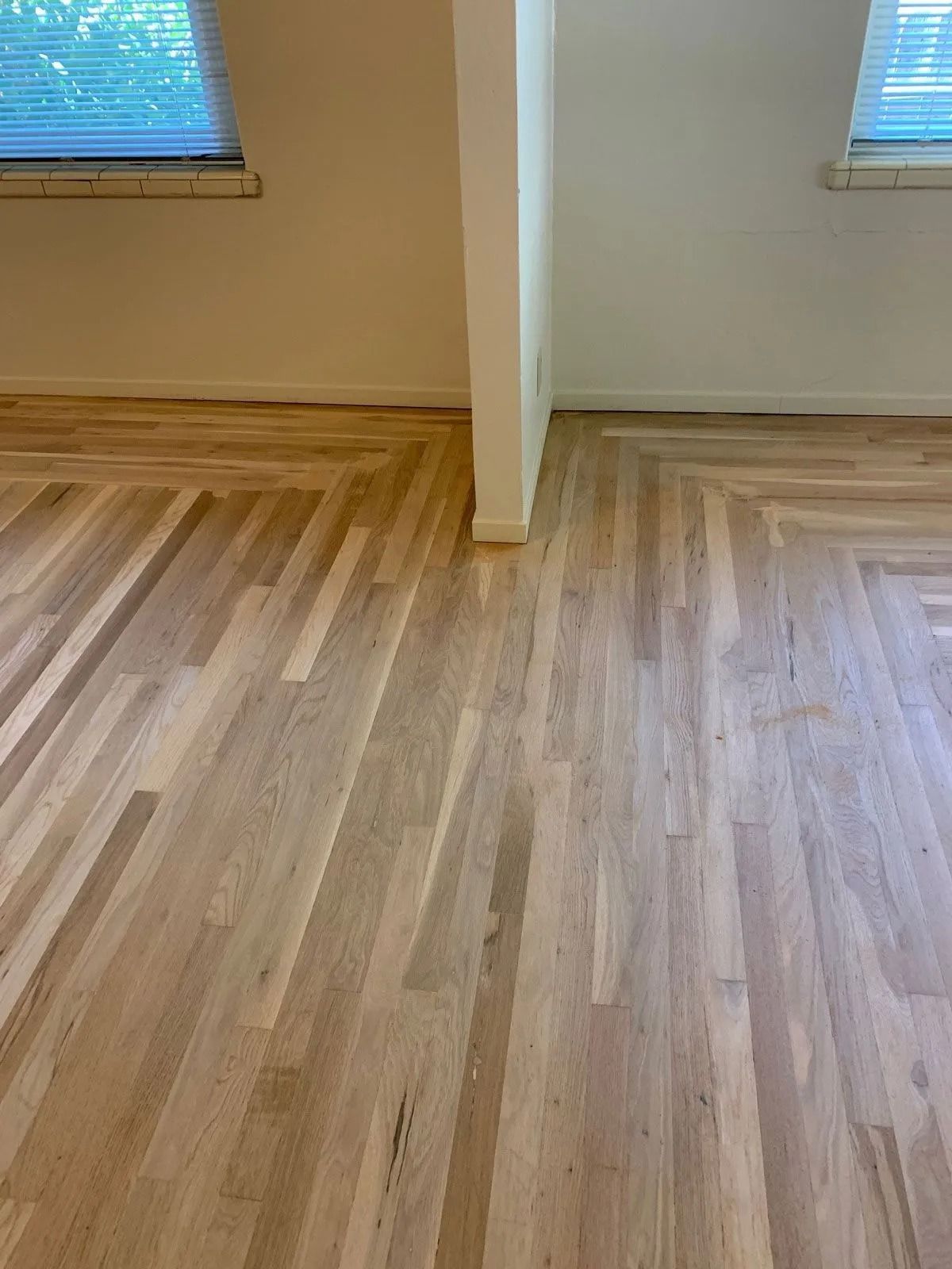Wooden parquet flooring in a room with white walls, and a dividing wall with two windows.