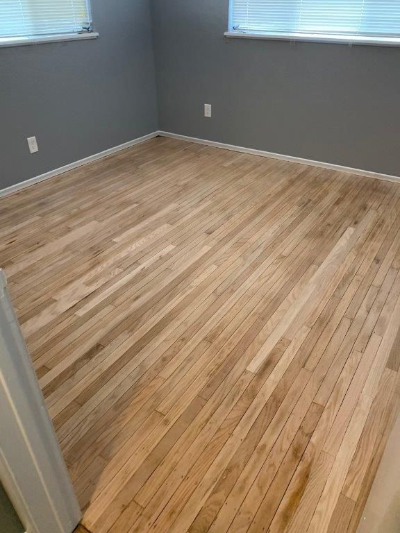 Empty room with wood floors and gray walls. Two windows at the top.