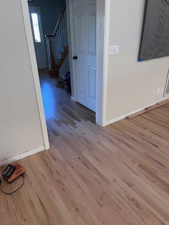 Hardwood floors in a home's entryway. A door, staircase, and neutral-colored walls are visible.