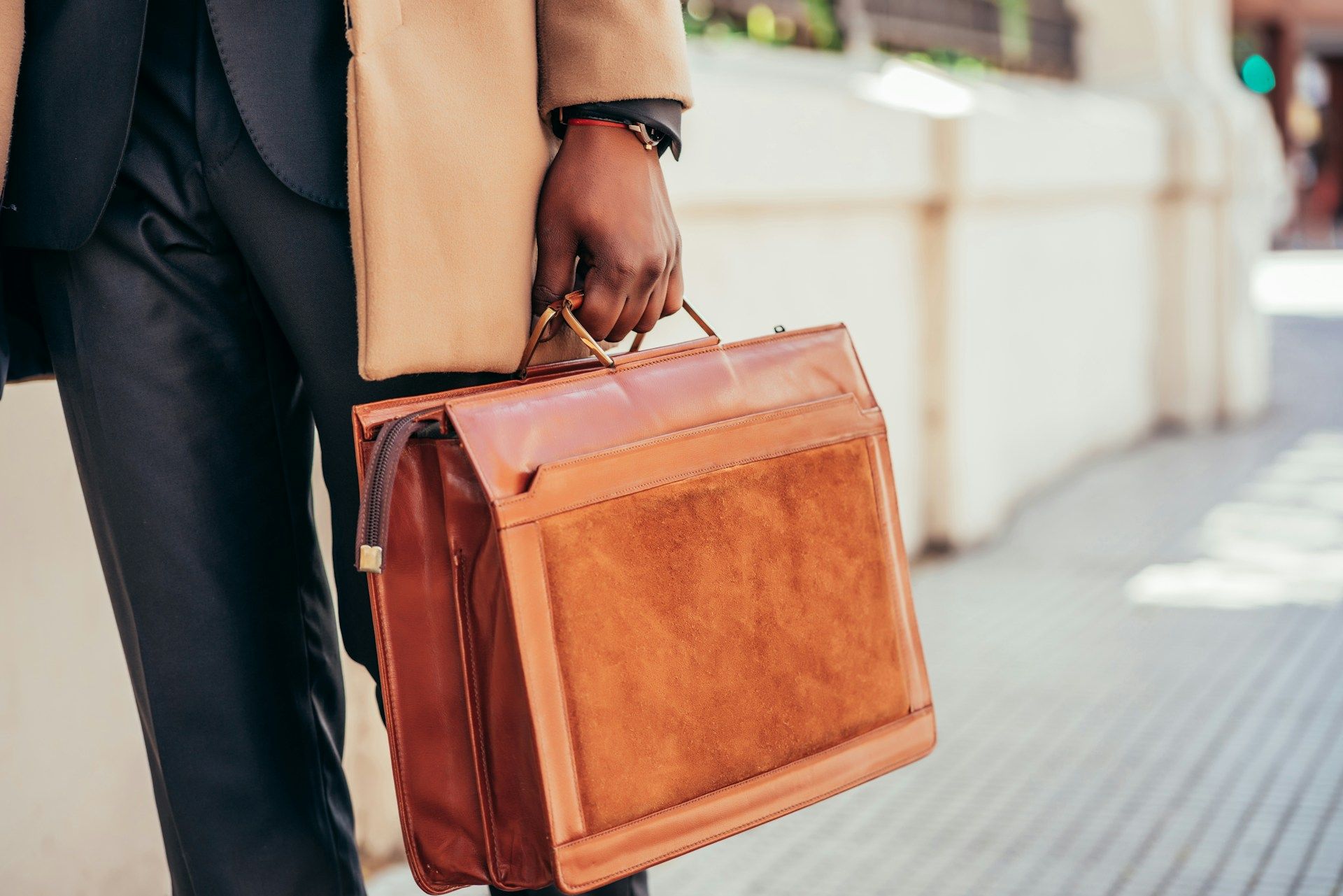 A man in a suit is holding a brown leather briefcase.