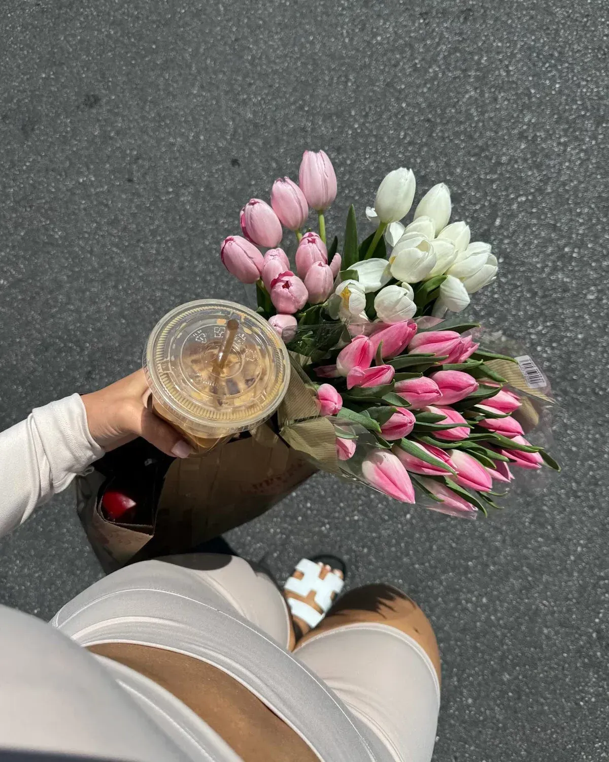Girl holding white, green and pink flowers on a walk with a iced latte in a white workout set