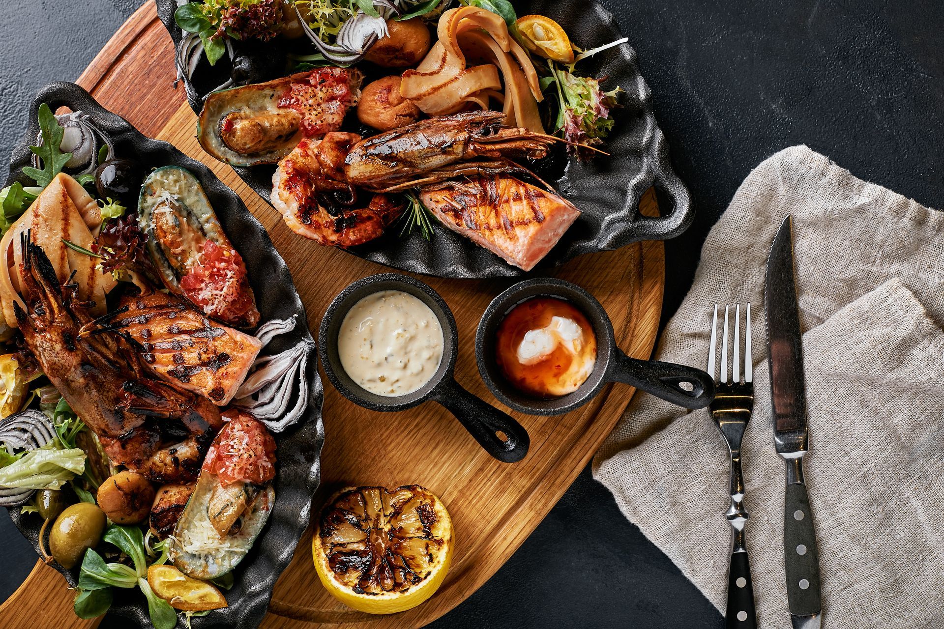 A wooden cutting board topped with plates of food and sauces.