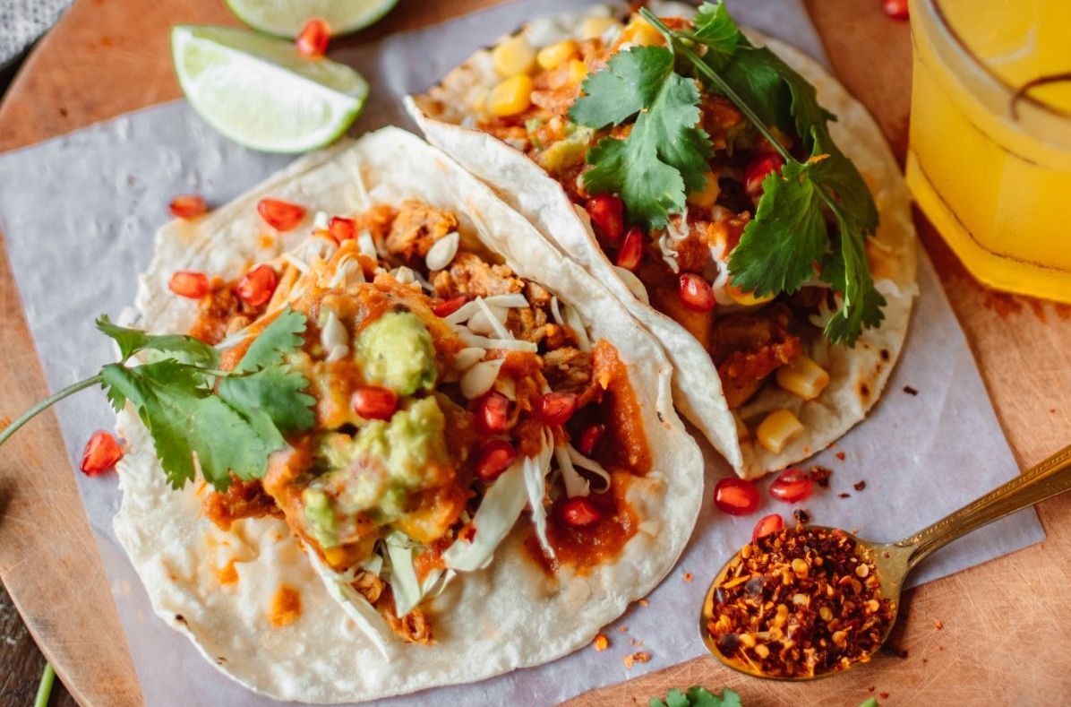 Two tacos are sitting on a wooden cutting board with a spoon of chili.