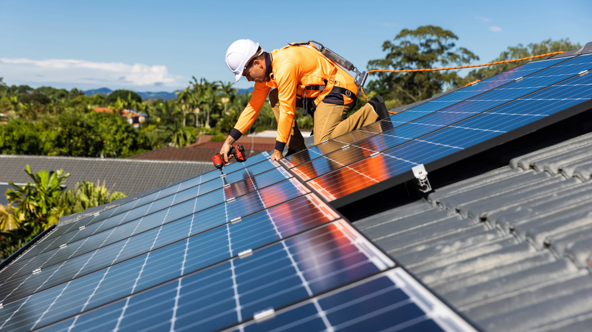 Installateur de panneaux solaires sur un toit, travaillant sur des panneaux solaires sous un ciel bleu.