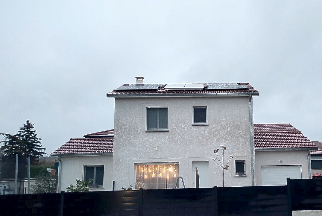 Une maison blanche avec un toit de tuiles rouges et des panneaux solaires sur le toit.