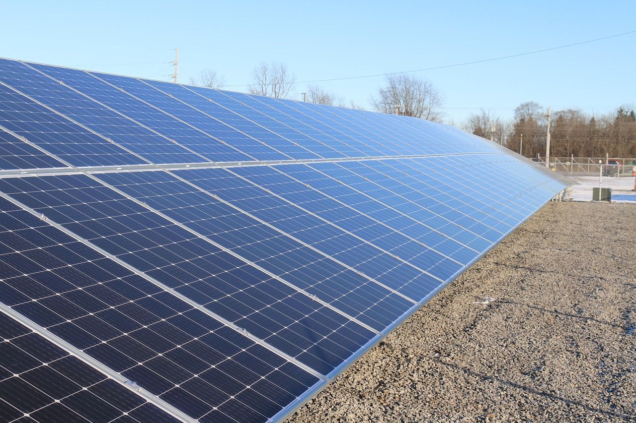 Des rangées de panneaux solaires dans un champ, sous un ciel bleu clair.