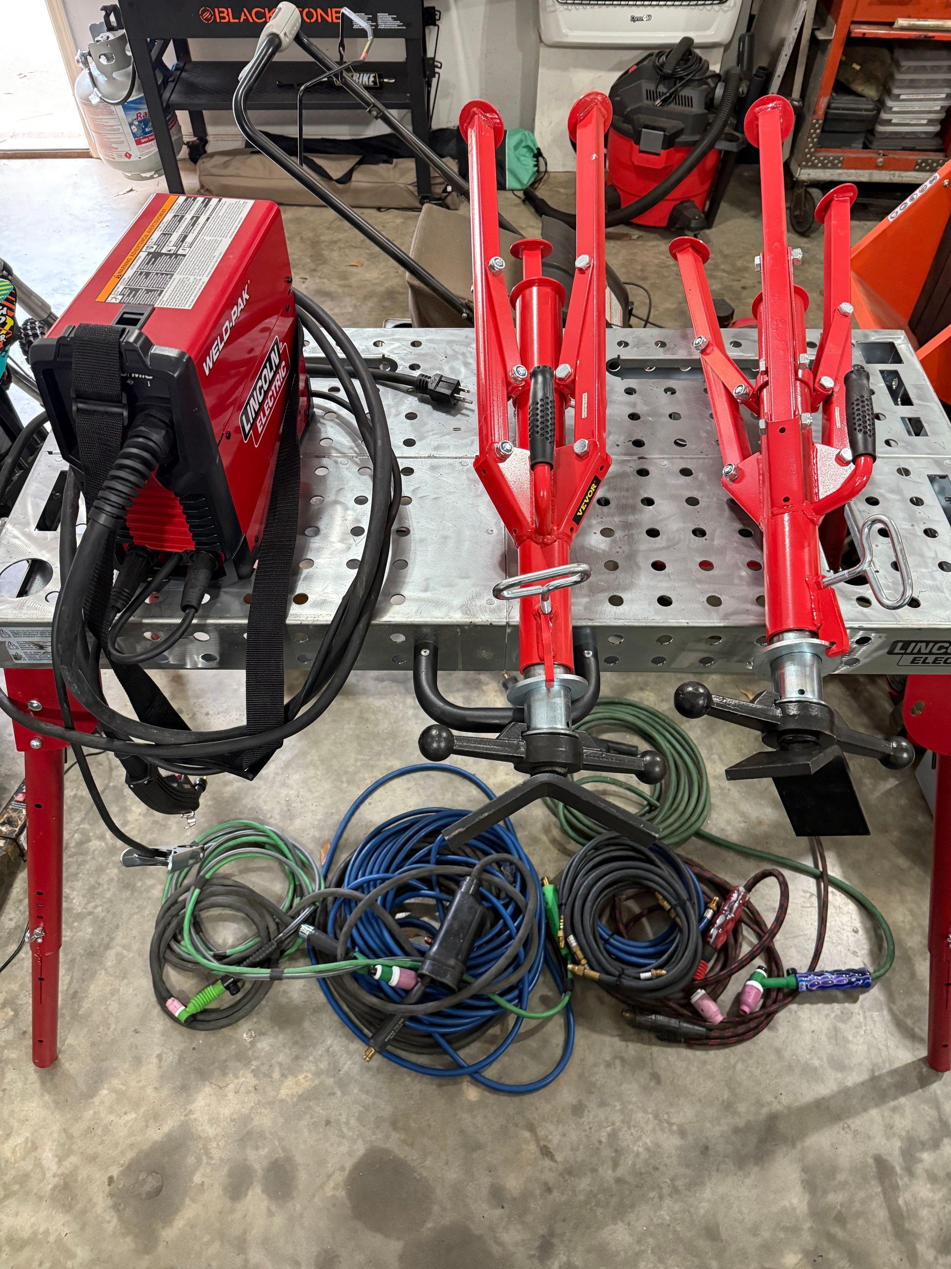 Red welding machine, TIG torches, cables, and tools on a metal welding table.