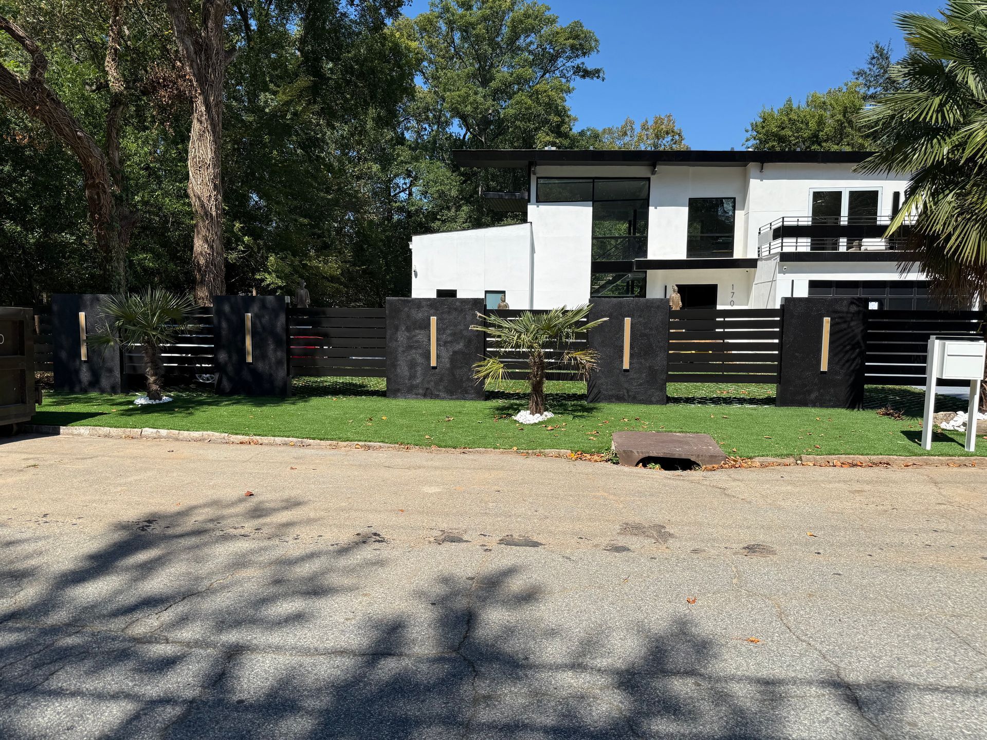 Modern white house with black accents, fronted by a black fence with gold accents and green lawn.