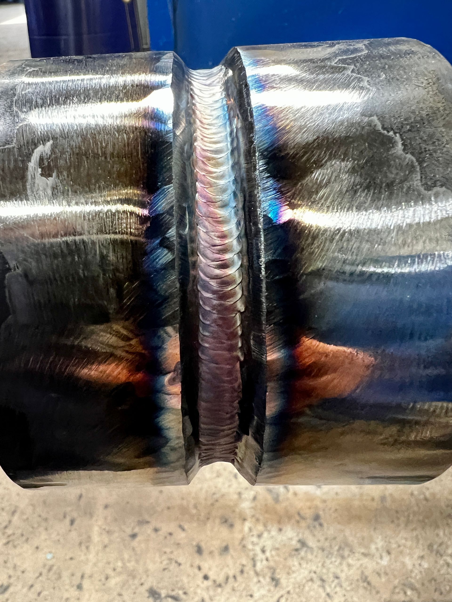 Close-up of a welded metal joint; dark with colorful heat-affected zones.