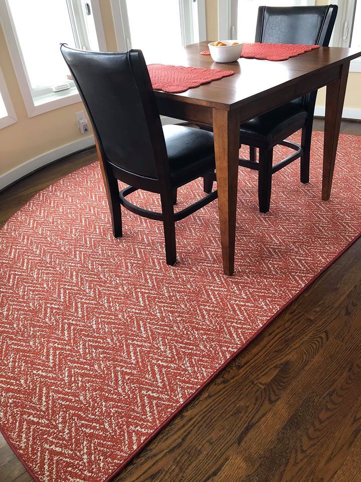 A dining room table and chairs with a red rug on the floor.