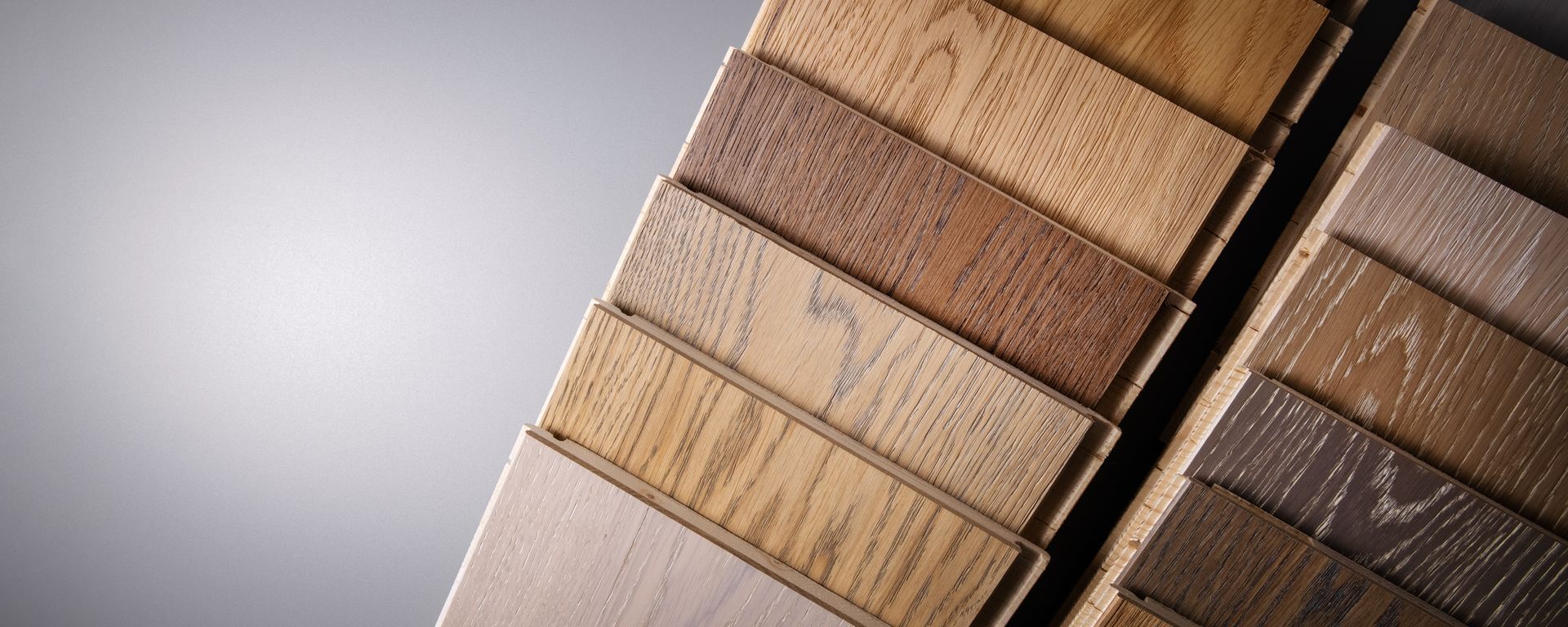 Stacked wooden flooring samples in various shades and grain patterns on display.