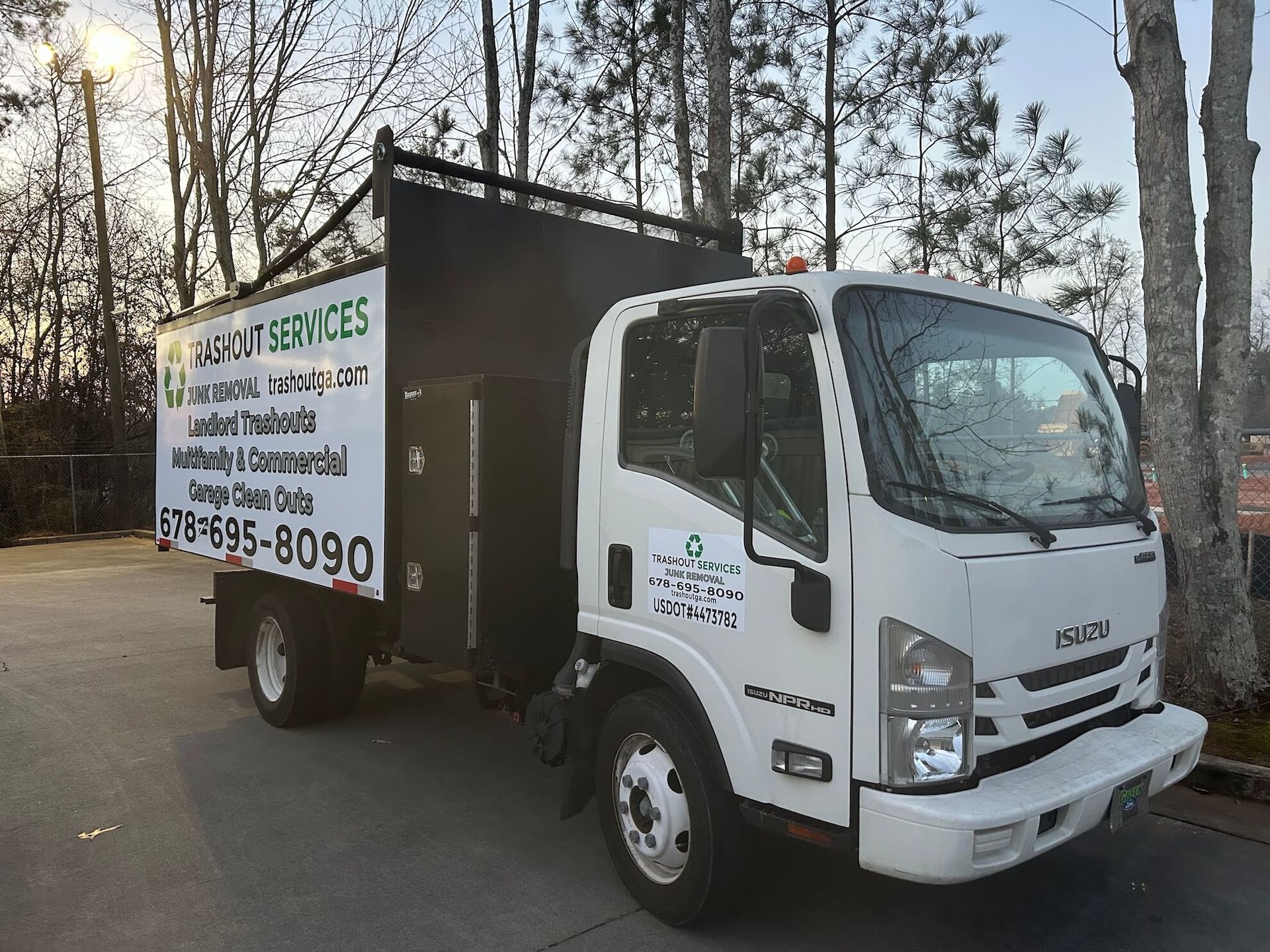White box truck with company signage parked outdoors on a tree-lined street.