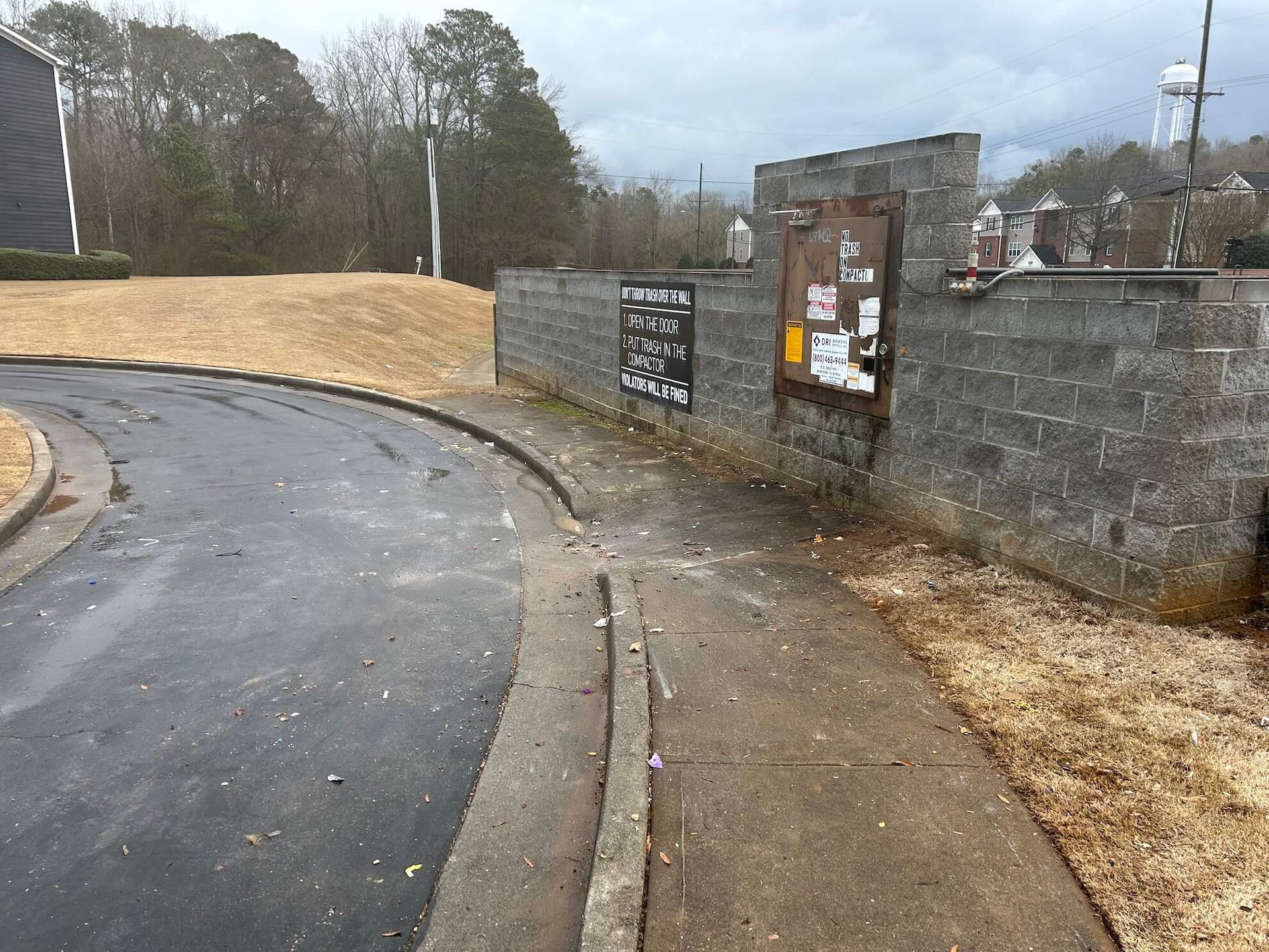Wet paved path beside a stone wall and signs on a cloudy day